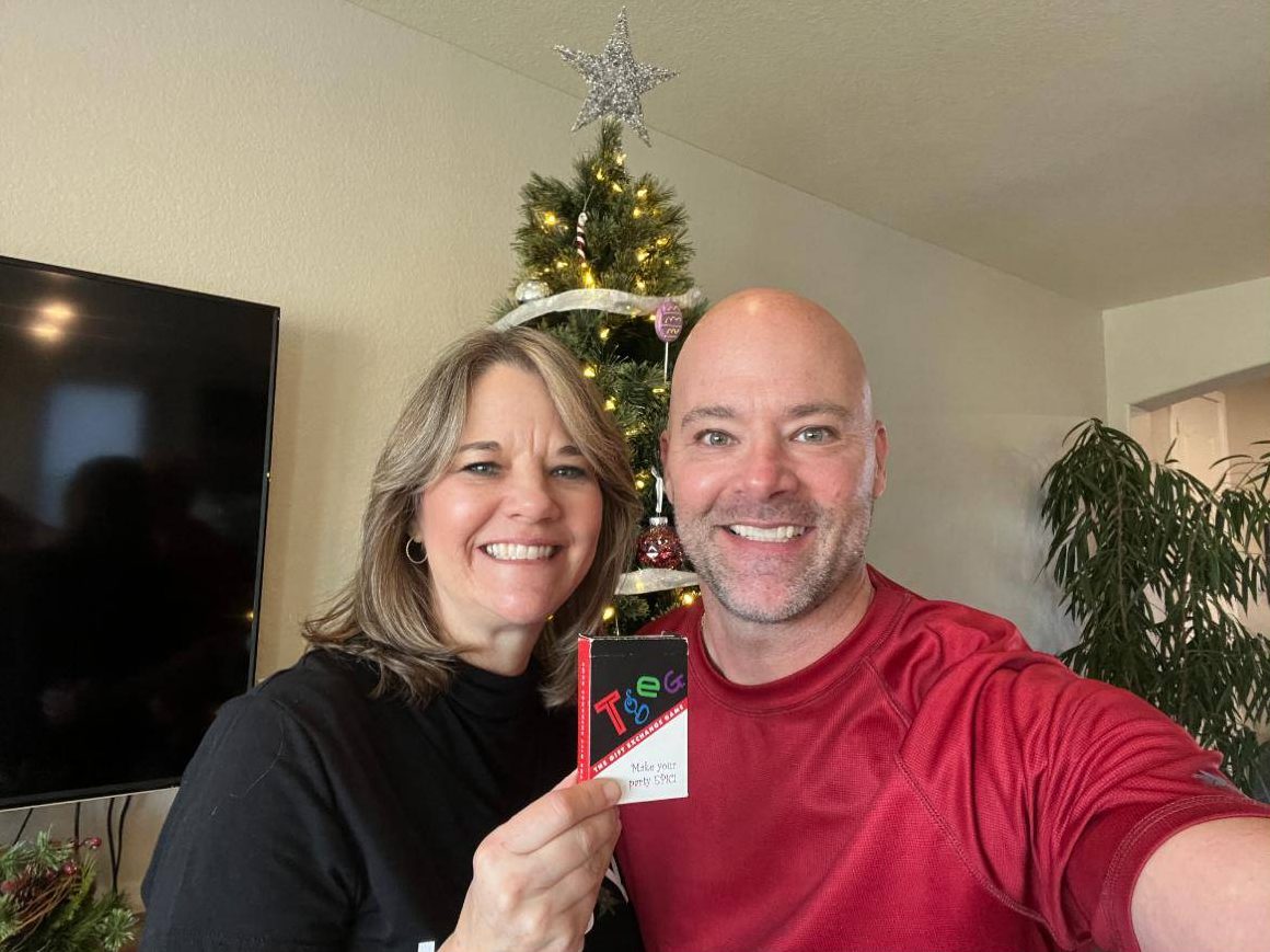 Kerrie and Eddie holding a TGEG deck in front of a Christmas tree